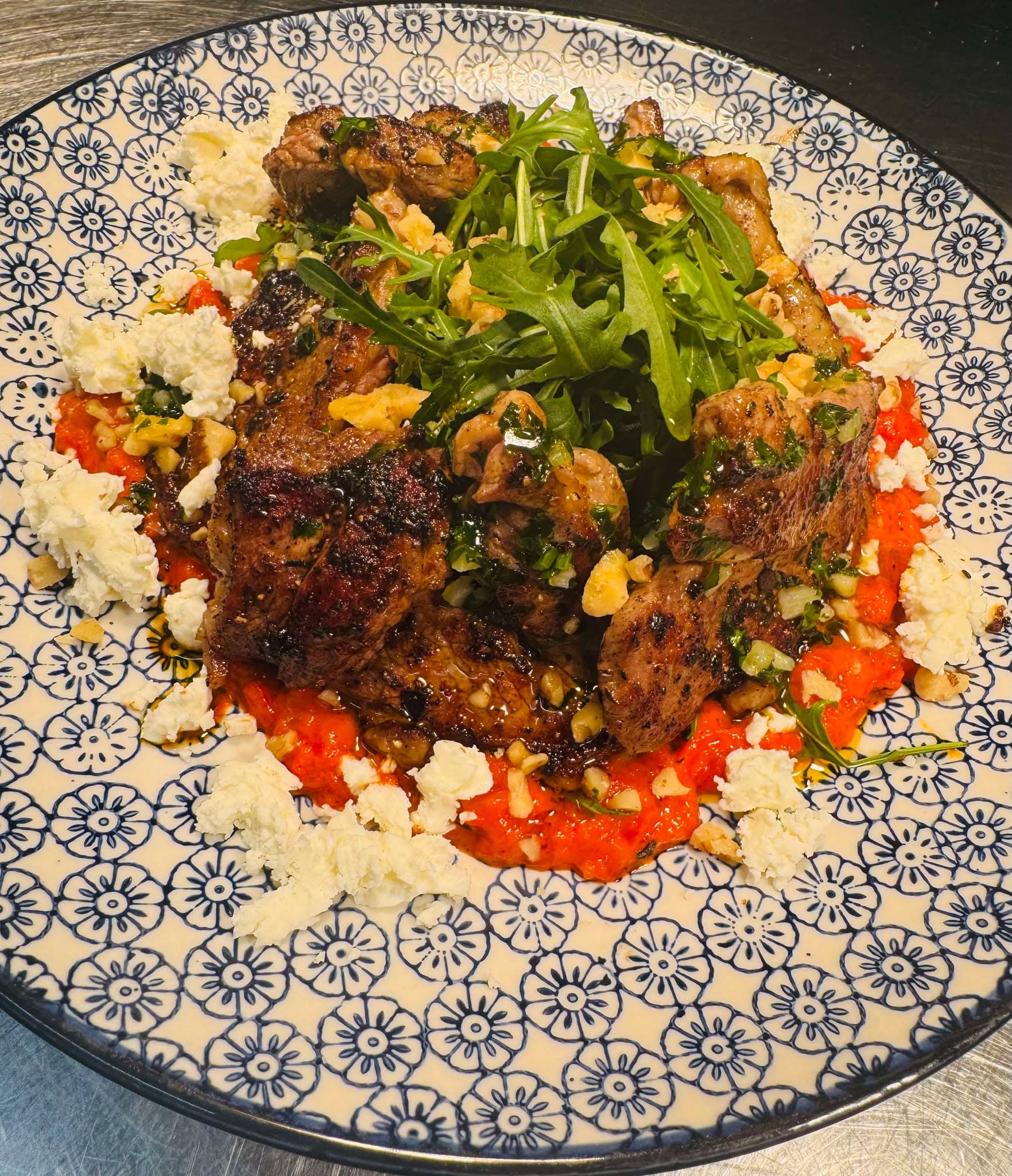 A richly spiced dark meat dish served over roasted red peppers and herbed couscous in a blue and white patterned bowl