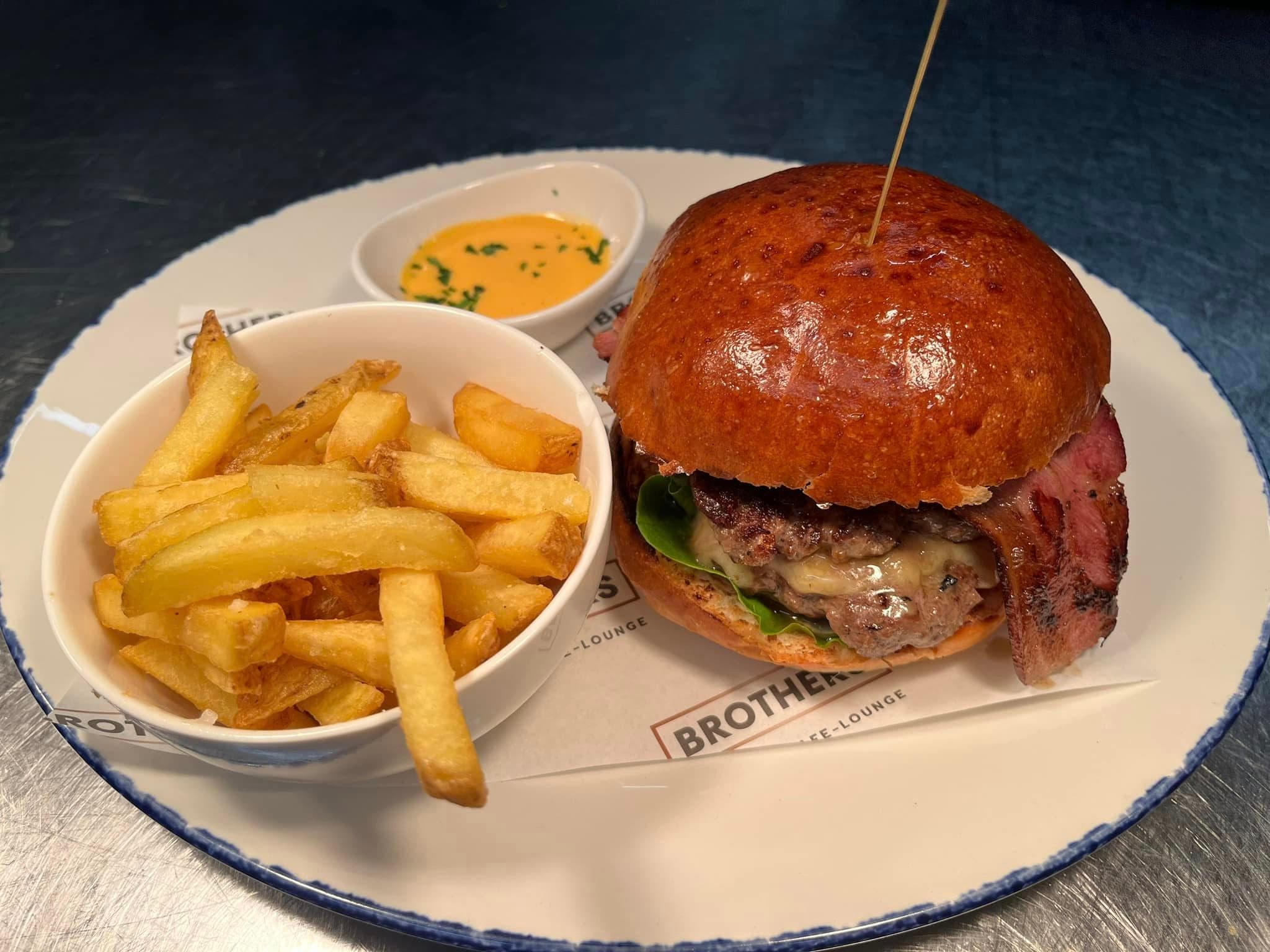A Brothers burger in a glazed brioche bun with house fries in branded paper and a pot of burger sauce