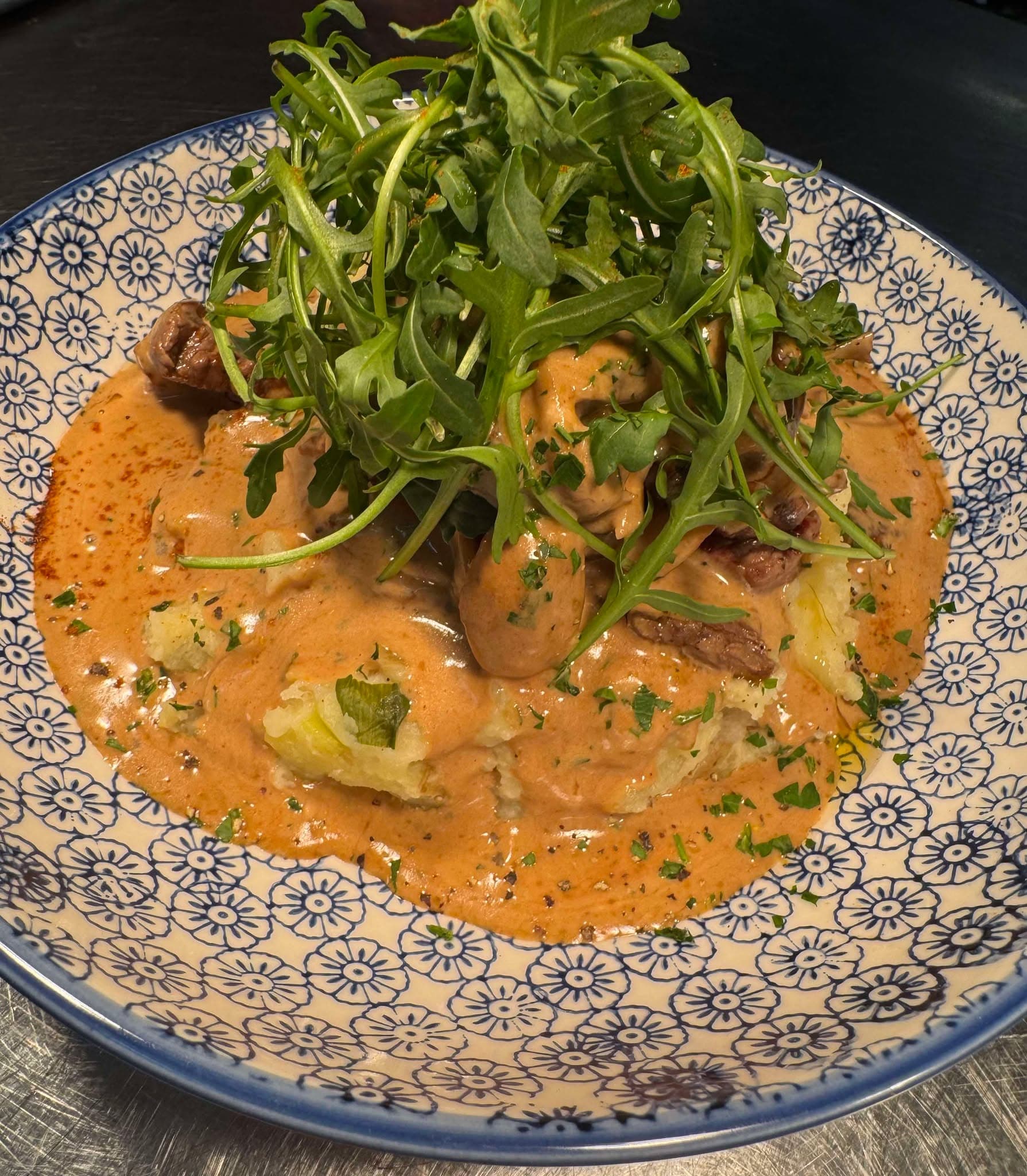 Chicken in a creamy paprika sauce under a pile of dressed rocket, in a blue and white patterned bowl
