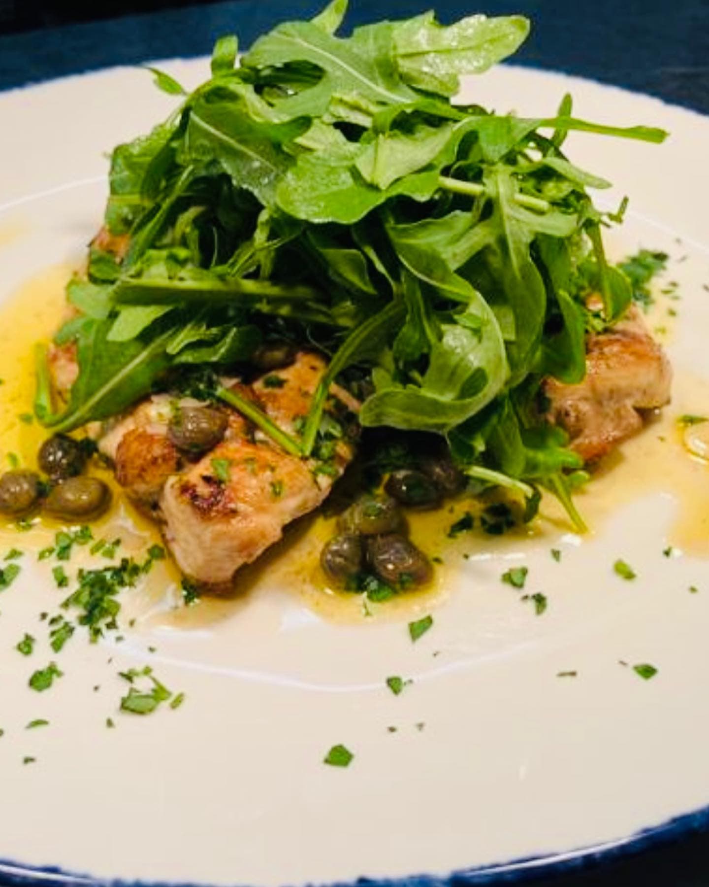 Seared scallops with a caper and herb dressing beneath a mound of dressed rocket