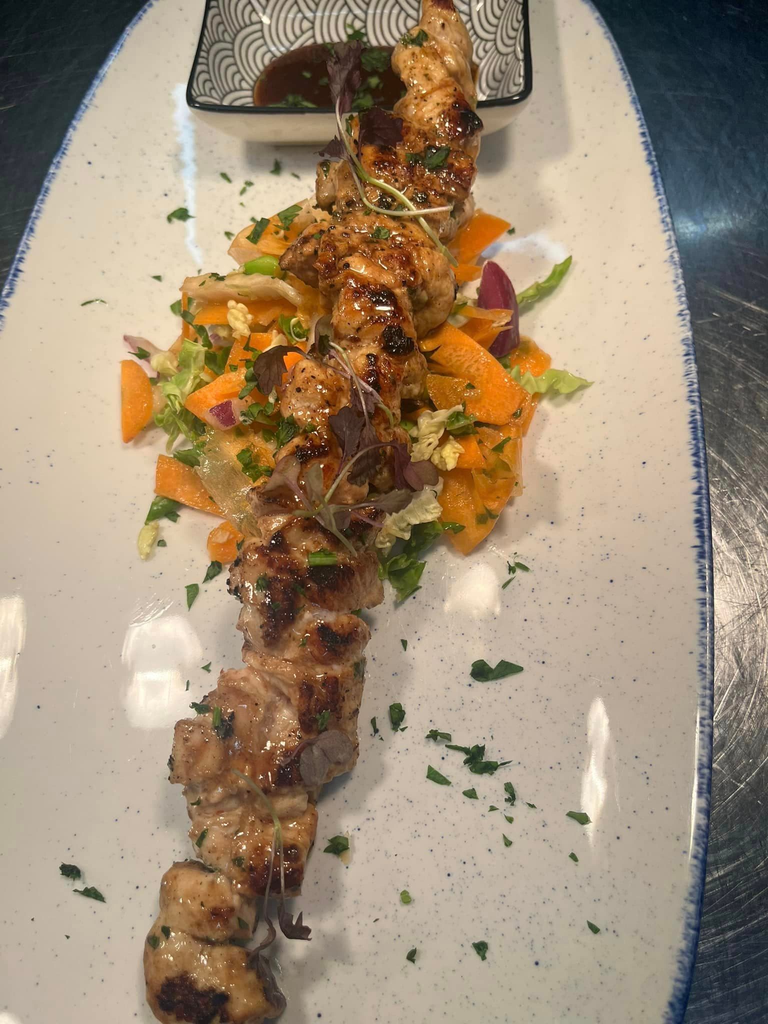A long grilled skewer topped with chopped tomato and herb salsa on a white plate