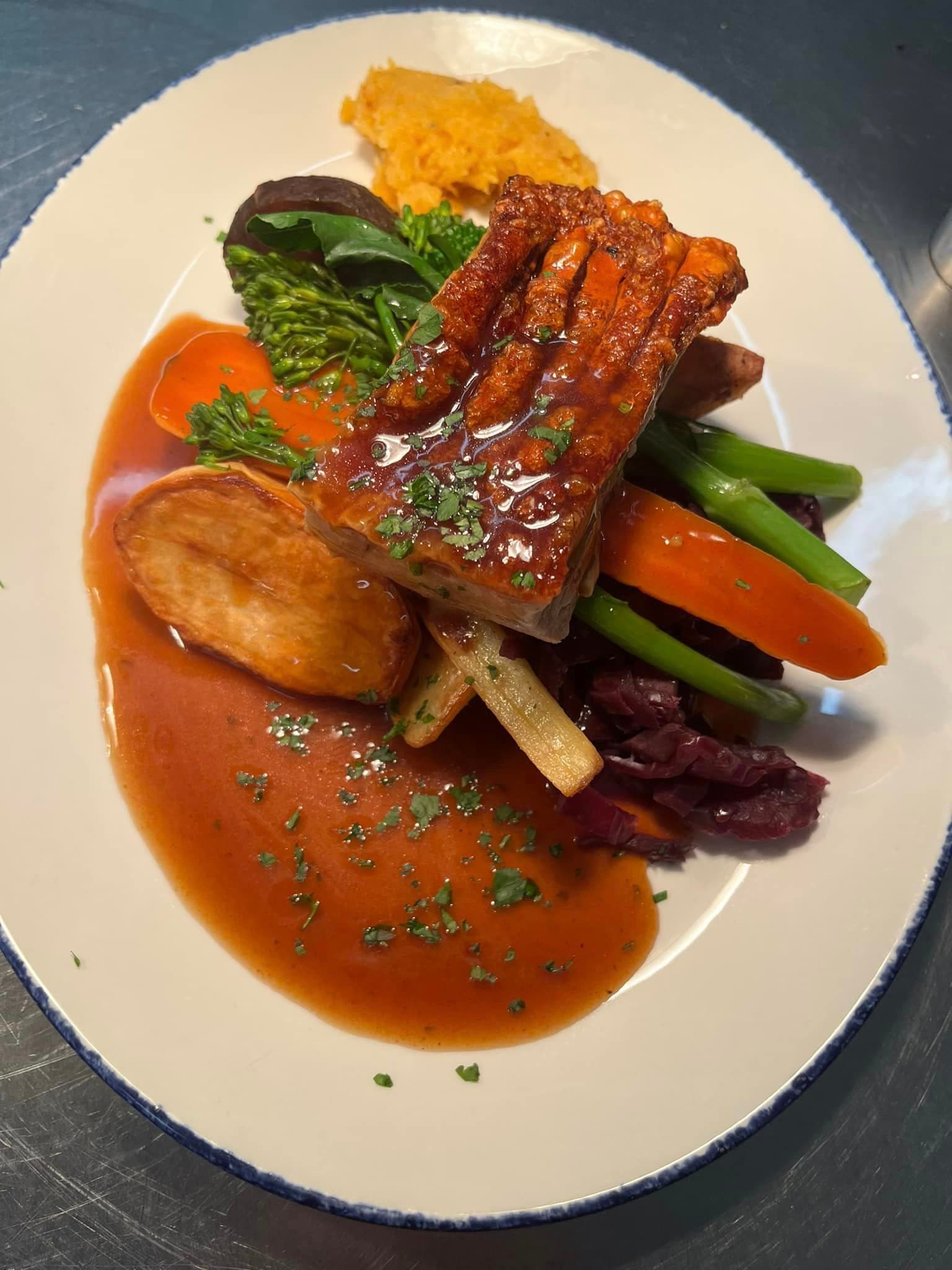 Crisp-skinned pork belly with roast potatoes, carrots, green beans, braised red cabbage and gravy