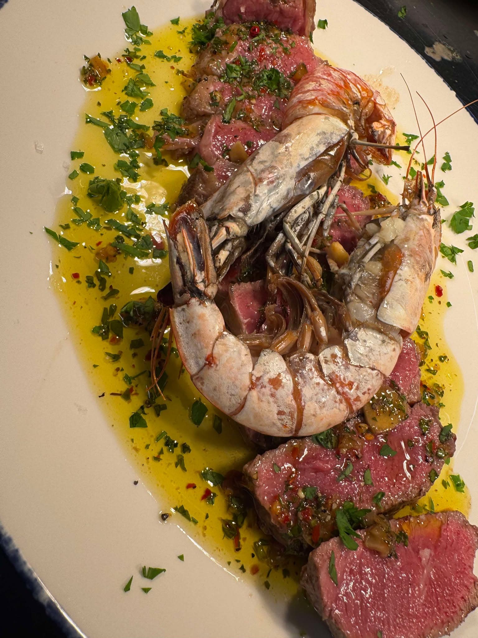 Sliced rump steak topped with chimichurri and whole grilled king prawns