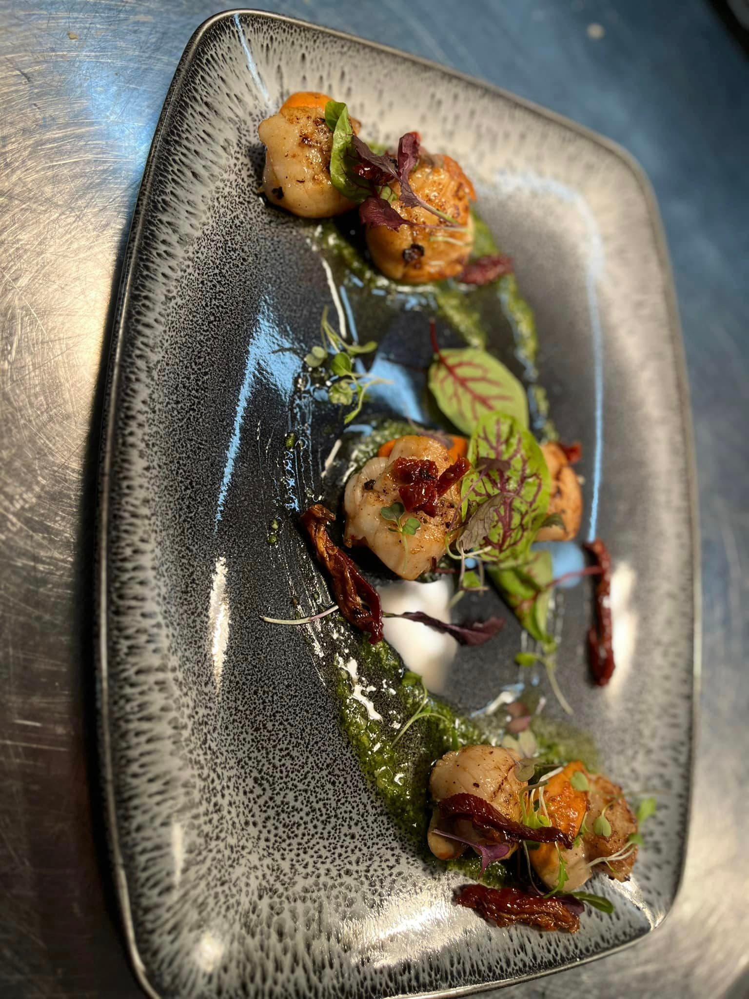 Seared scallops with herbs and a dark dressing on a grey plate