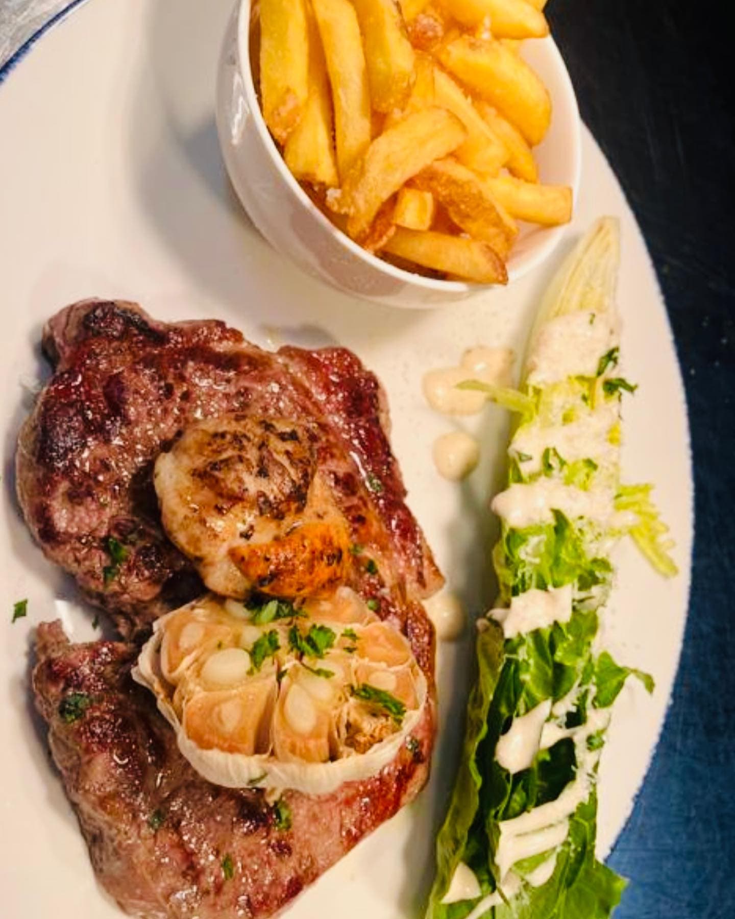 A rump steak topped with a seared scallop and half a roasted garlic bulb, with house fries and a dressed cos wedge