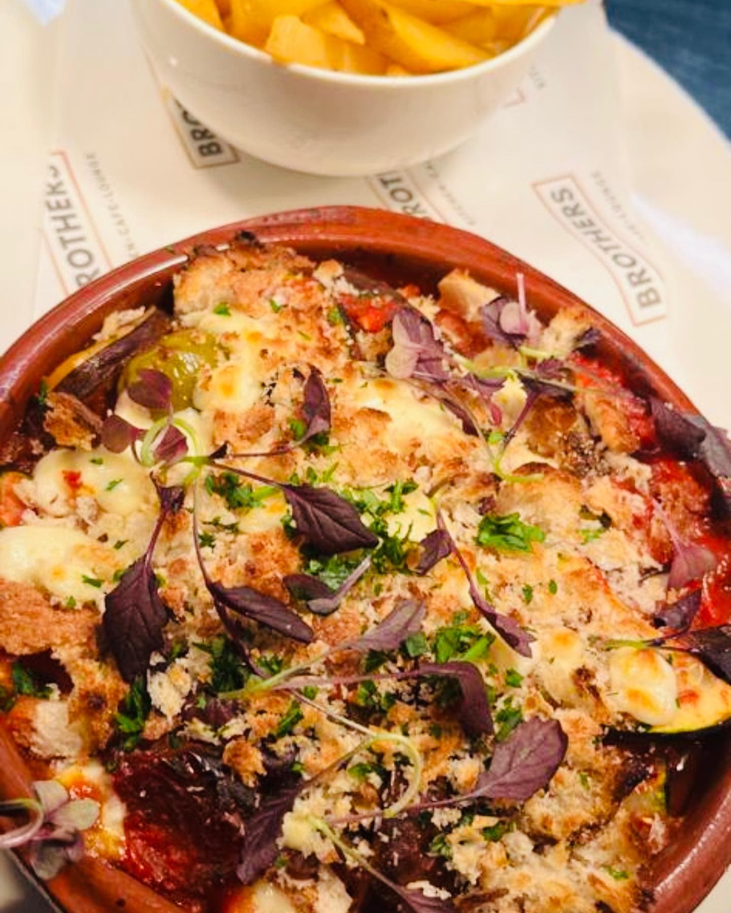 A baked dish of mozzarella, tomato, aubergine and basil in a terracotta dish