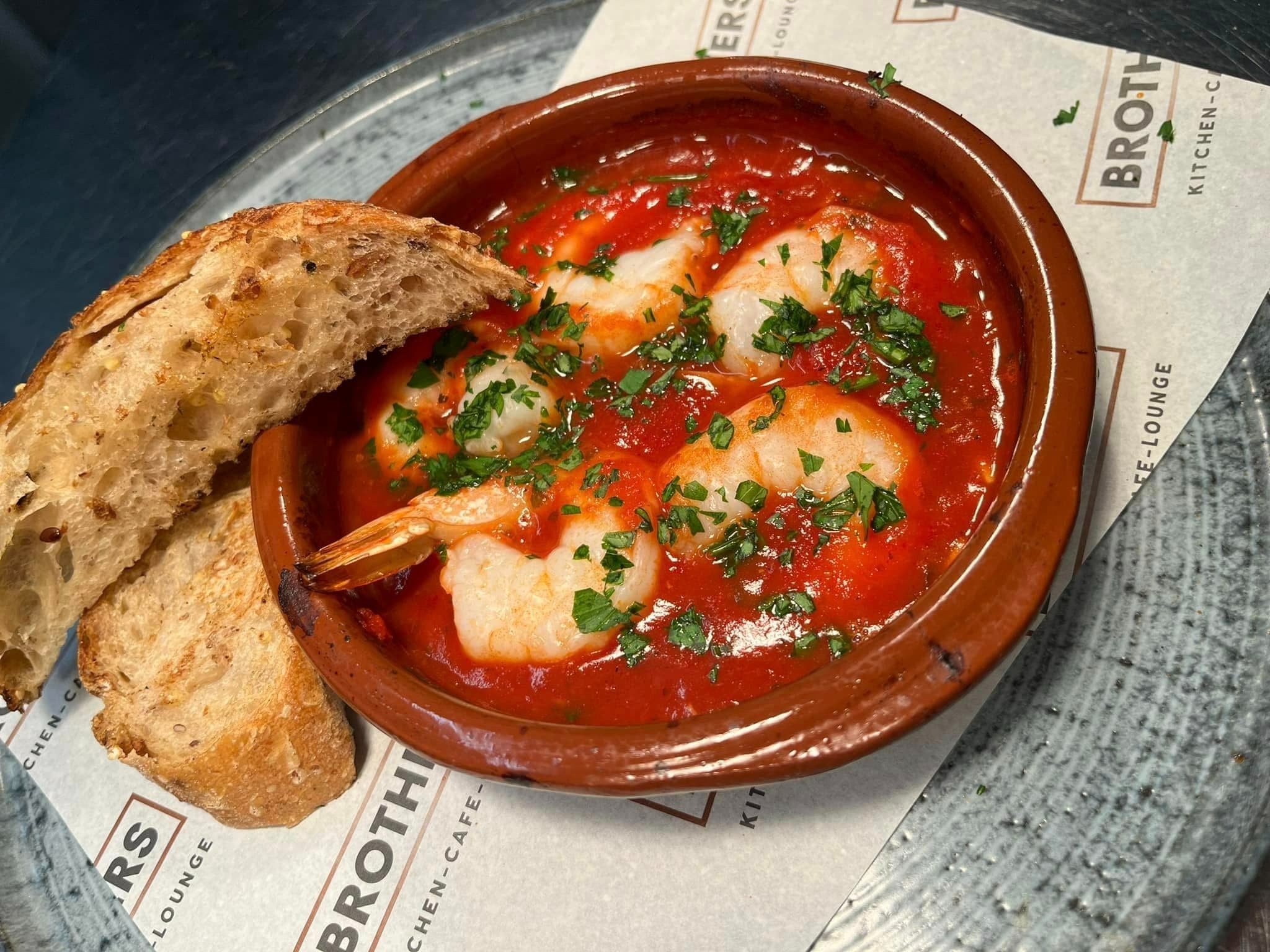 King prawns in a rich tomato sauce in a terracotta dish with toasted sourdough